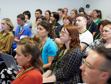 A group of people at an event seated and listening to a presentation being given.