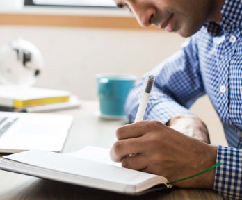 Person with laptop writing in a notebook.