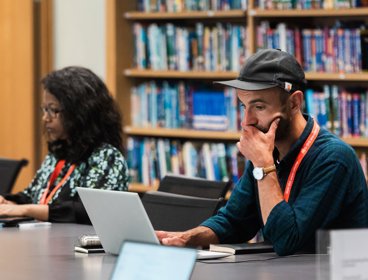 Two people using laptops while seated at a table in a library.