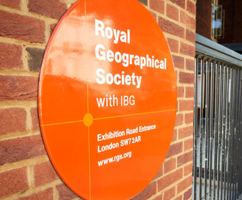 Sign on the outside of the Society's building close to the entrance, with three people walking in.