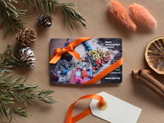 A membership card wrapped up in orange ribbon on brown wrapping paper with festive foliage surrounding it, including acorns, holly and cinnamon sticks.
