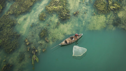 Person in a traditional fishing boat next to a green barrier reef.