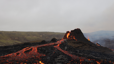  A volcano slips glowing red, yellow and black glowing lava onto a progressivly charred hilly grassland