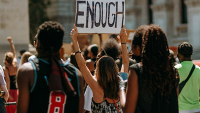 A group on people protest in the middle of the street with a one individual holding a sign that says 'enough'.