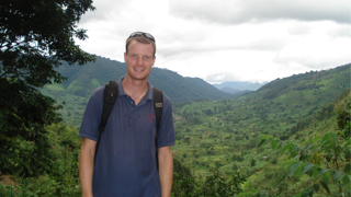 PhD student in navy blue short stood against backdrop of forests in Uganda.