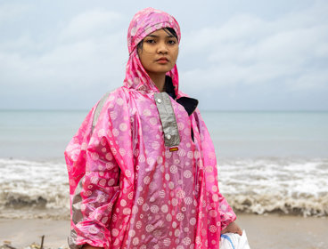 Person standing on a beach in Bali wearing a bright pink plastic raincoat.