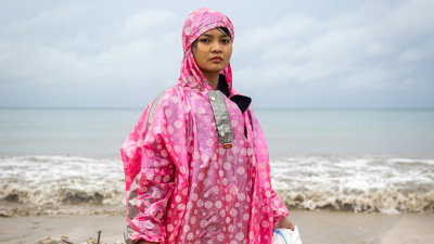 Person standing on a beach in Bali wearing a bright pink plastic raincoat.