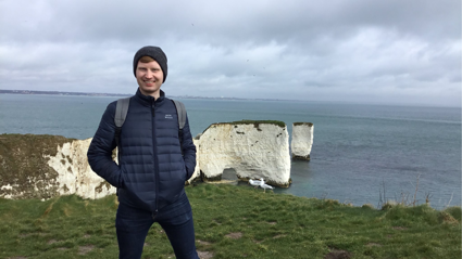 Paul Logue posing on a cliffside with white chalk cliffs in the background leading into the sea.