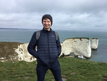 Paul Logue posing on a cliffside with white chalk cliffs in the background leading into the sea.