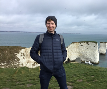 Paul Logue posing on a cliffside with white chalk cliffs in the background leading into the sea.