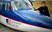 A woman standing next to a small plane that has the words Ordnance Survey written on the side.