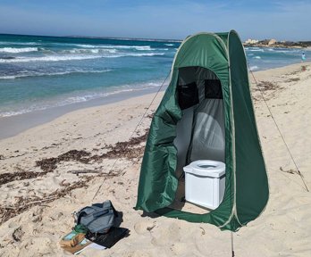 A tent with a portable toilet in, located on a beach.