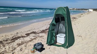 A tent with a portable toilet in, located on a beach.