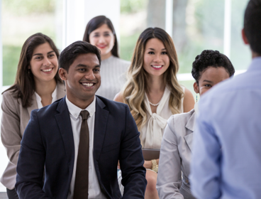 Group of smartly dressed people listening to person talk.
