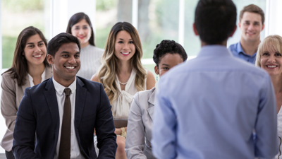 Group of smartly dressed people listening to person talk.