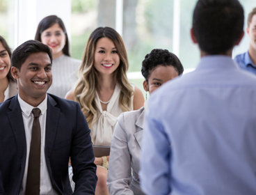 Group of smartly dressed people facing a person with their back facing the camera.