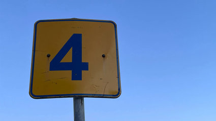 A yellow and black sign showing the number 4 on a blue sky background.
