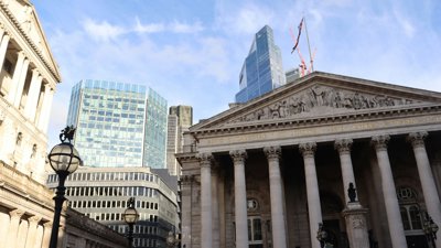 The Bank of England building with a flag of the Union Jack with a backdrop of skyscrapers.