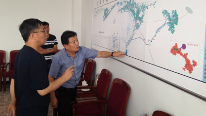 Three people looking and pointing at a large map pinned to a wall.