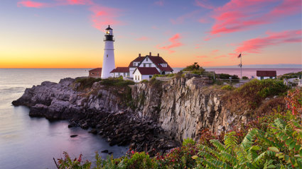 A house and lighthouse on a cliff at sunset.