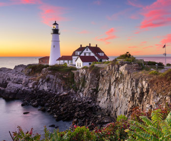 A house and lighthouse on a cliff at sunset.
