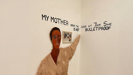 Art installation with the text 'my mother opens the door at 7am she is not bulletproof' on a white wall.
