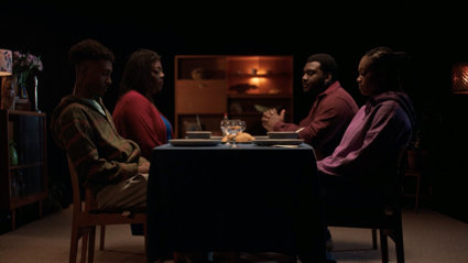 Four people sit around a dimly lit dining table.