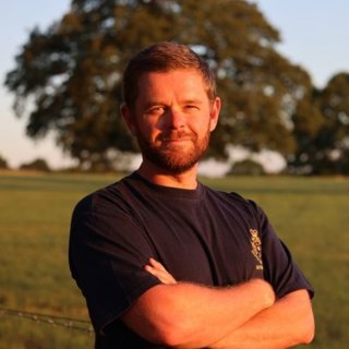 Zack Coleman standing in a field of grass with a large tree behind him.
