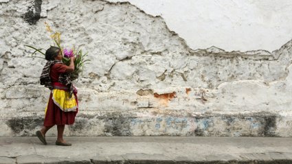 A woman carries a basket of flowers next to the cobblestone streets and crumbling walls of Antigua Guatemala.