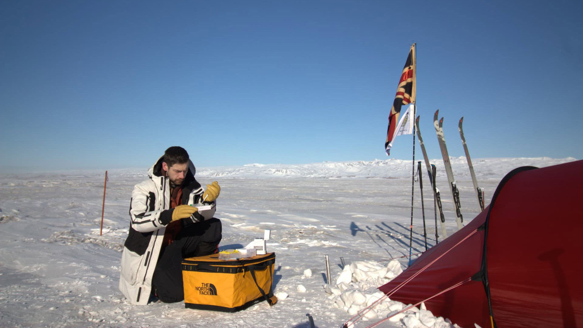A researcher sauatted next to a tent testing samples in an arctic region.