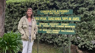 Woman standing in a front stating that she has arrive at Uhura Peak in Tanzania.