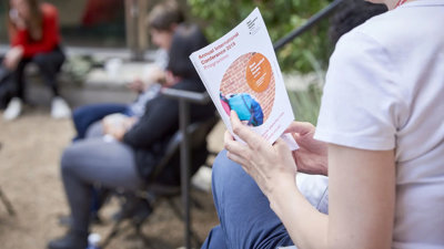 A person sat down outside holding a borchure. The front page reads 'Annual International Conference 2019 Programme'.