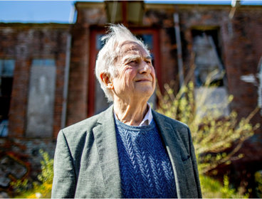 Person wearing jumper and suit looking out against backdrop of industrial building.