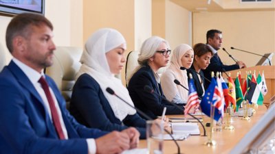 Delegates at an international conference sat at a wooden table with microphones and flags in front of them.
