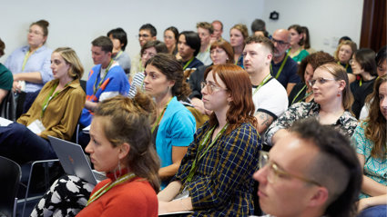 A group of people at an event seated and listening to a presentation being given.