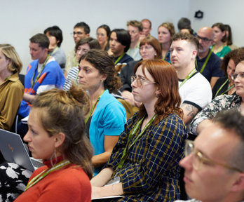 A group of people at an event seated and listening to a presentation being given.