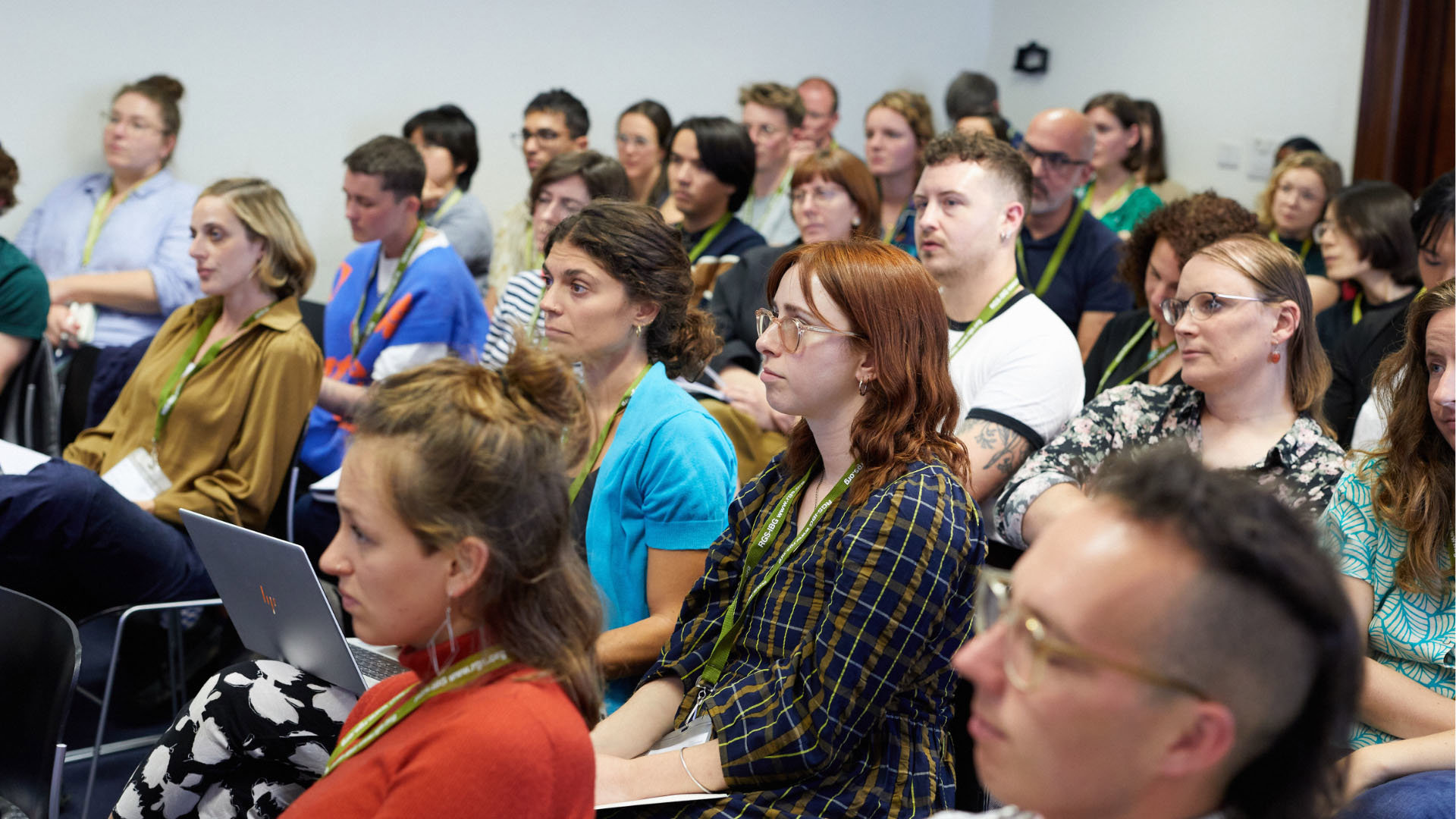 A group of people at an event seated and listening to a presentation being given.
