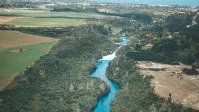 Aerial view of a winding blue river cutting through green forest and farmland with a town in the distance.