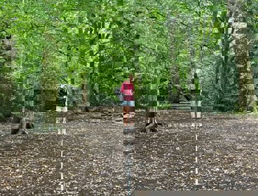 Person in a forest holding a long rope, standing slightly away from the camera.