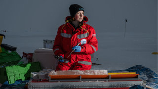 Researcher on a boat in the Arctic taking temperature measurements from an ice core.