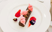 A chocolate torte topped with pink meringue and served with red sauce and edible flowers.
