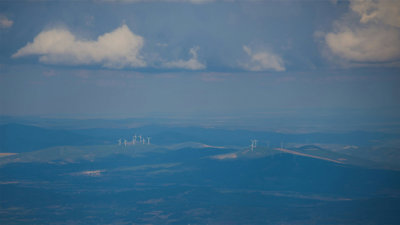 A landscape in hues of blue with groups of wind turbines on hills in the distance.