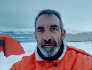 Dave Connell standing in front of an orange tent, surrounded by snow. 