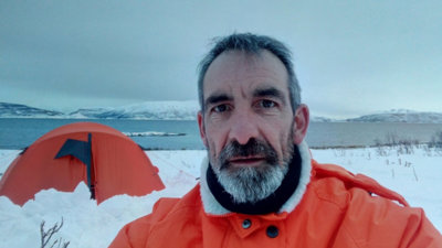 Dave Connell standing in front of an orange tent, surrounded by snow. 
