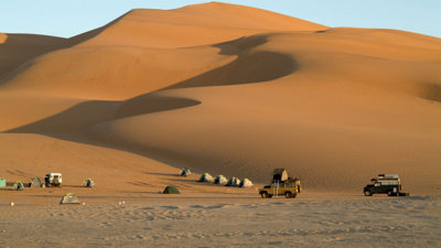An expedition camp set up in the desert against a backdrop of high sand dunes.