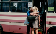 Two family members standing next to a bus hugging each other.