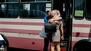 Two family members standing next to a bus hugging each other.
