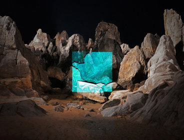 A red rock formation at night with a blue square projected on to it. Photograph titled 'Chuam Rock 2021'. 