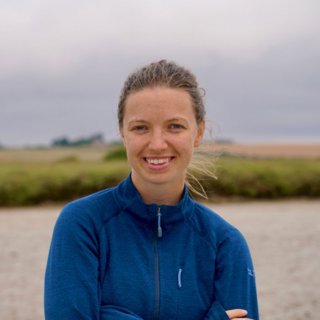 Rosalind Chaston, smiling, wearing a blue zip up jumper and crossing her arms.