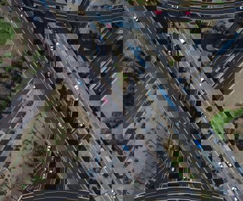 An aerial view of a motorway junction showing the roads crossing each other in an attractive pattern. Some roads are straight, others are curved. Each has multi coloured cars on it.